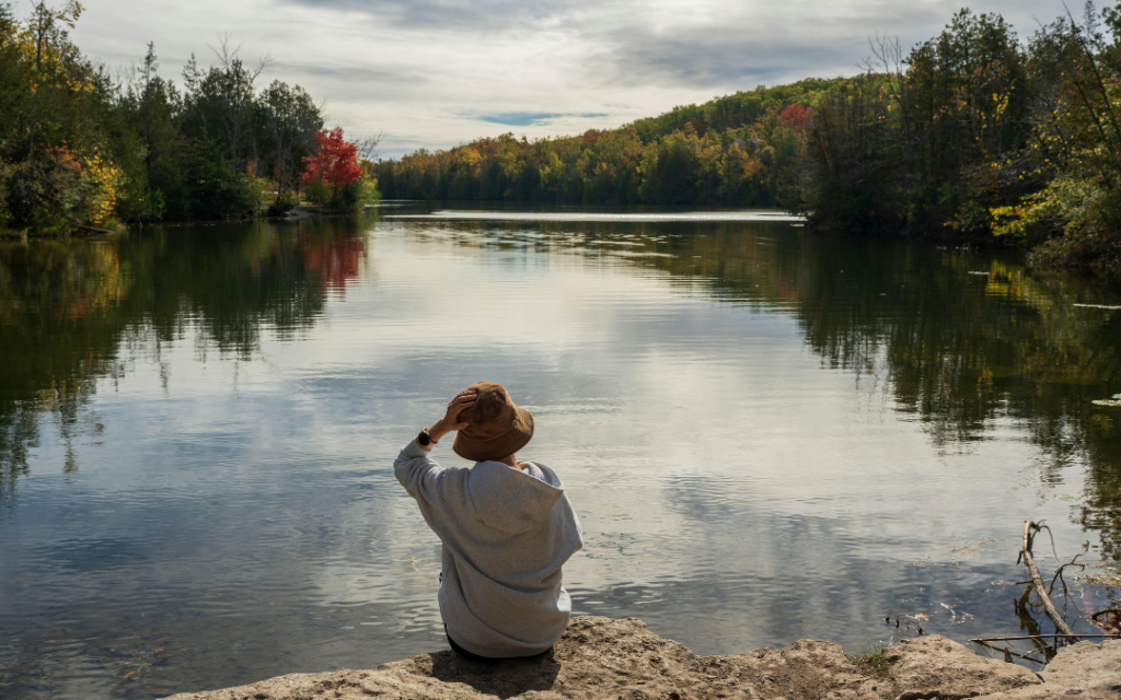 Person sitting at edge of a lake in the fall looking out over the lake